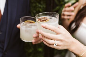 two white people's hands holding cocktails in old fashioned glasses