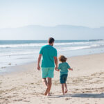 Dad and child holding hands and walk together. Father and son walking on summer beach.