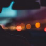 Out of focus street at night, seen over the shoulder of a driver in a car.