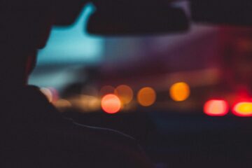Out of focus street at night, seen over the shoulder of a driver in a car.