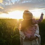 Mother and daughter standing in a field with a sunset behind them.