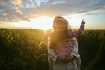 Mother and daughter standing in a field with a sunset behind them.
