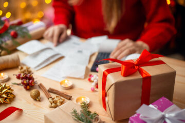 Holiday themed table with a person looking over bills and financial documents, with a calculator handy.
