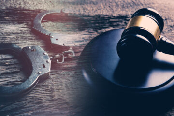 Photo of a gavel and handcuffs on a wooden surface.
